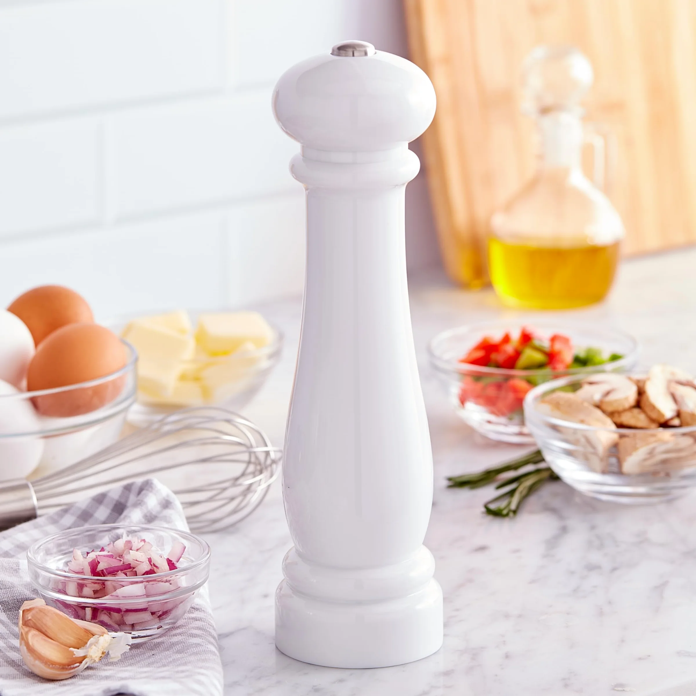 The white Kamenstein Traditional Glossy battery grinder on a marble counter, the push button on top of its knob.