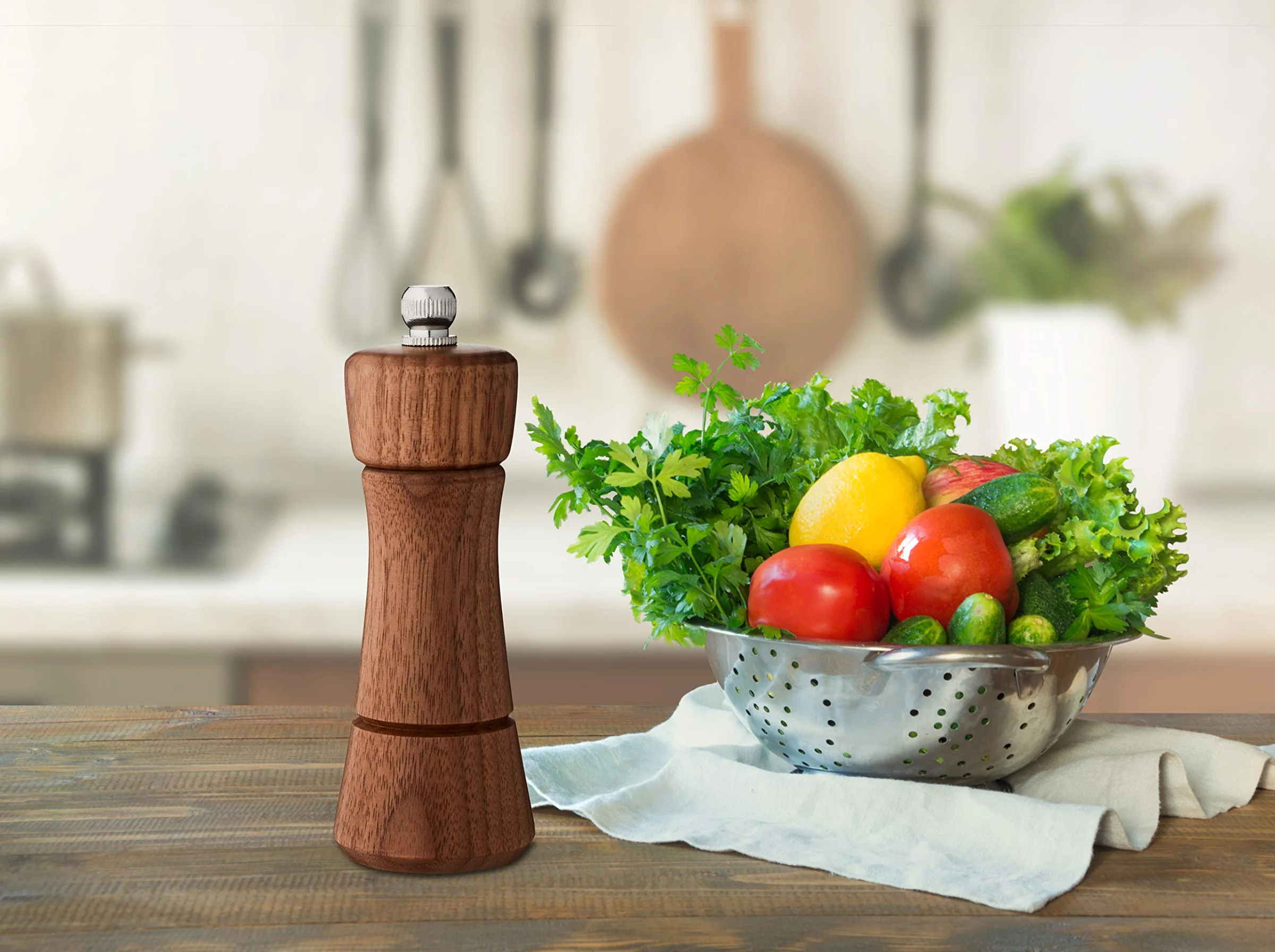The Nottingham walnut pepper grinder on a kitchen table, beside a colander of vegetables.
